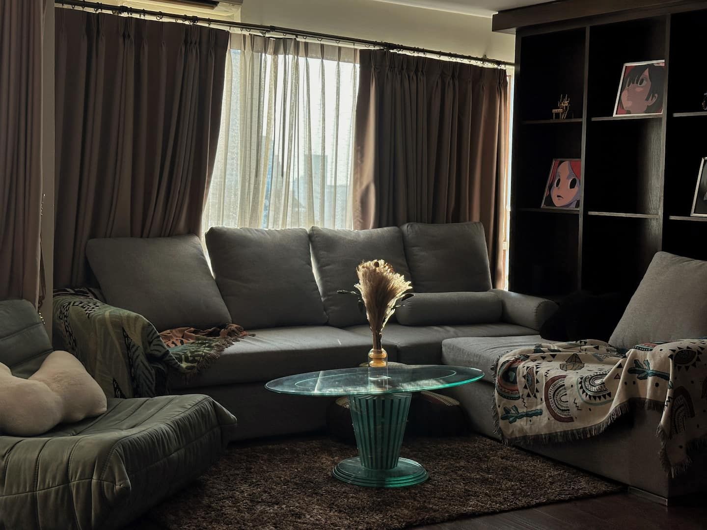 A living room with a sectional sofa, a glass coffee table, and a bookshelf with framed pictures.