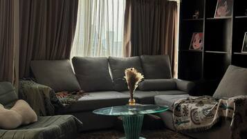 A living room with a sectional sofa, a glass coffee table, and a bookshelf with framed pictures.
