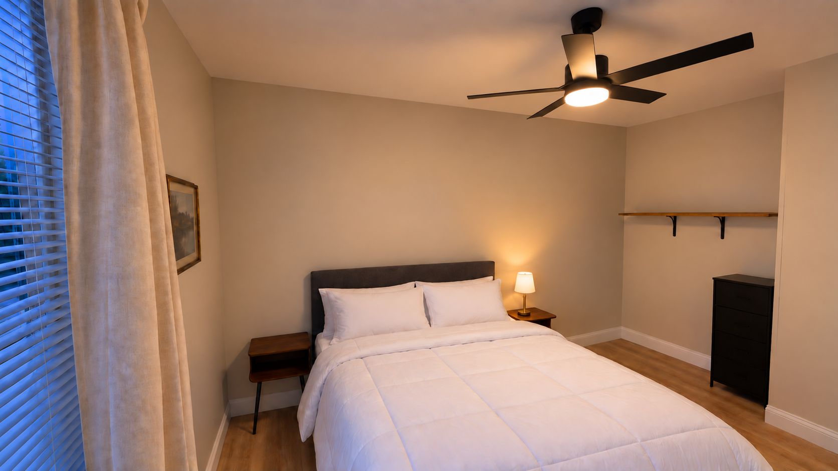A bedroom with a bed, bedside table, lamp, ceiling fan, and a window with blinds.