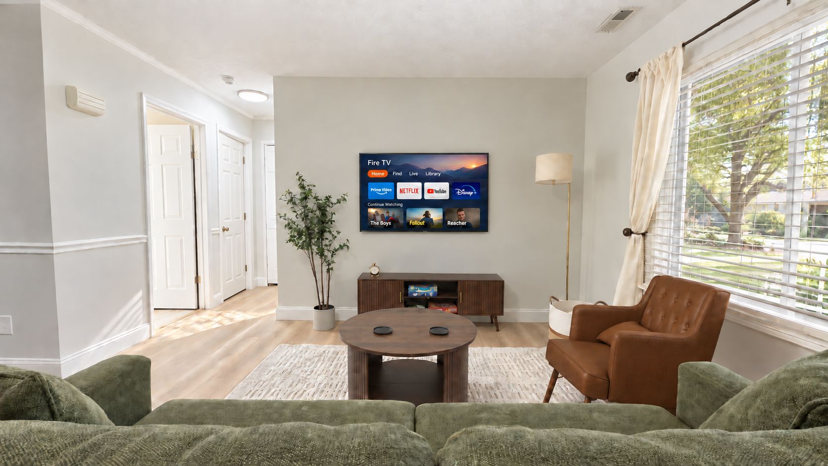 A living room with a flat-screen TV mounted on the wall, a brown leather armchair, and a green sofa.