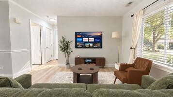 A living room with a flat-screen TV mounted on the wall, a brown leather armchair, and a green sofa.