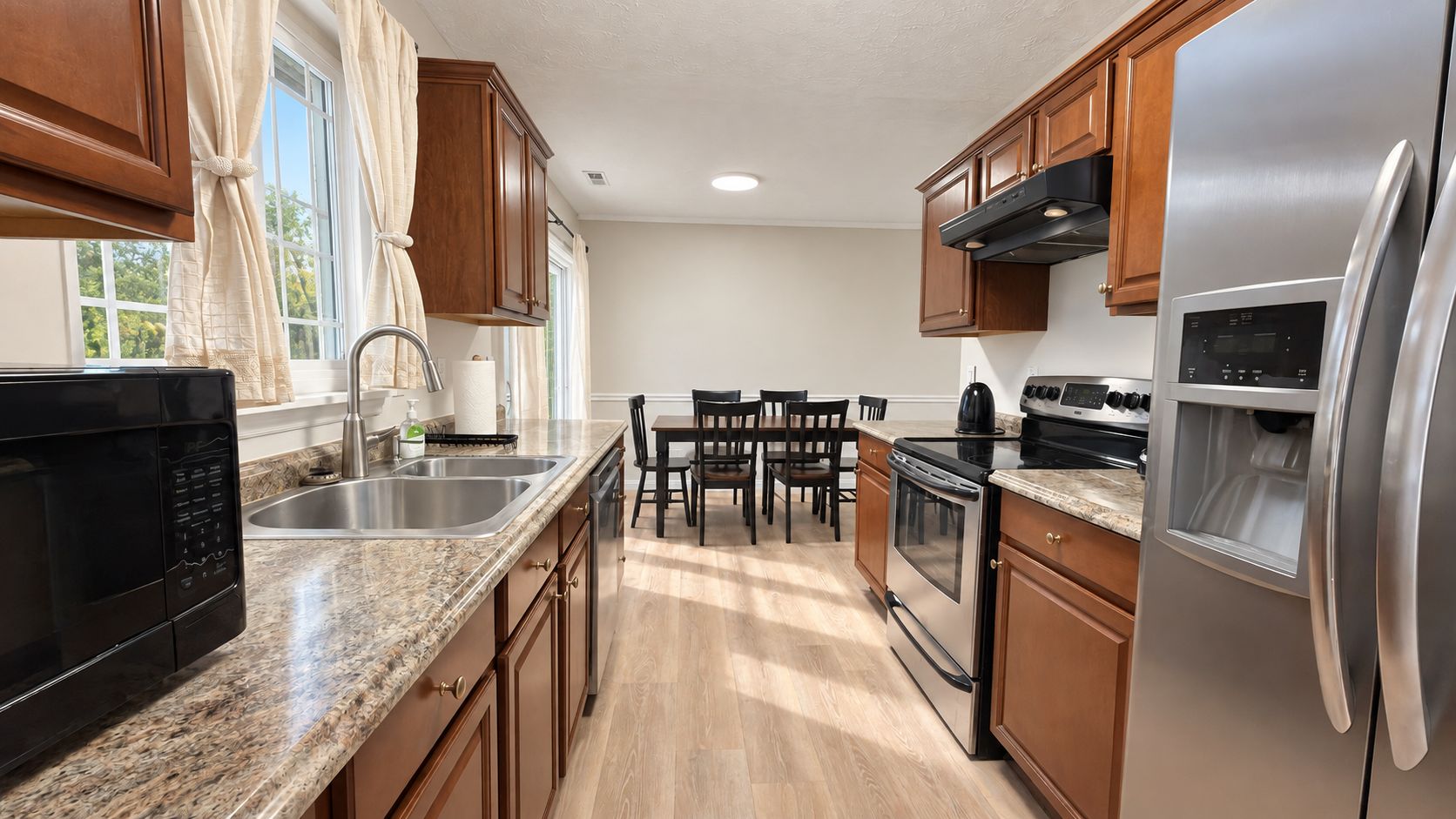 A modern kitchen with stainless steel appliances, wooden cabinets, and a granite countertop.