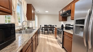 A modern kitchen with stainless steel appliances, wooden cabinets, and a granite countertop. - Family Home Near NC State Fair & Downtown Cary Park - Live Like a Local! (Cary)