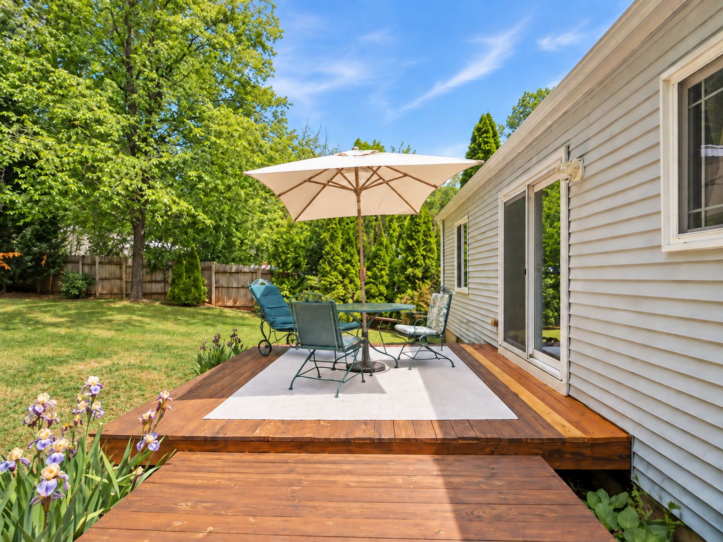 A wooden deck with a table and chairs, an umbrella, and a house with a sliding door.