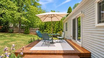 A wooden deck with a table and chairs, an umbrella, and a house with a sliding door.