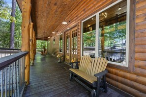 A wooden cabin with a porch, a bench, and a view of the surrounding forest. - Whispering Meadows|Fooseball|Firepit (Broken Bow)