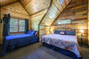 Quarto de cabana com duas camas, uma janela e uma luminária em uma mesa de cabeceira.