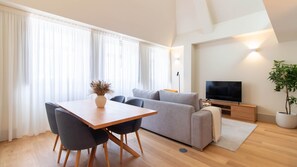 Ein modernes Wohnzimmer mit einer Couch, einem Fernseher, einem Esstisch, Stühlen und einer Topfpflanze.