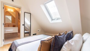 Ein Schlafzimmer mit Dachfenster, einem Bett mit Kissen, einem Nachttisch und einem Spiegel.