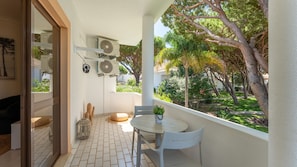 A balcony with a table and chairs, a potted plant, and a view of a garden with trees and shrubs. - Falésia Stylish 2BR W/Balcony & Pool by LovelyStay (Olhos de Água)