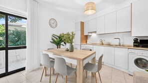 A modern kitchen with white cabinetry, a wooden dining table, and a built-in washing machine. - Falésia Stylish 2BR W/Balcony & Pool by LovelyStay (Olhos de Água)