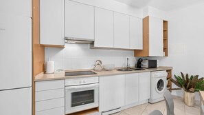 Una cocina moderna con armarios blancos, horno empotrado, lavadora y microondas.