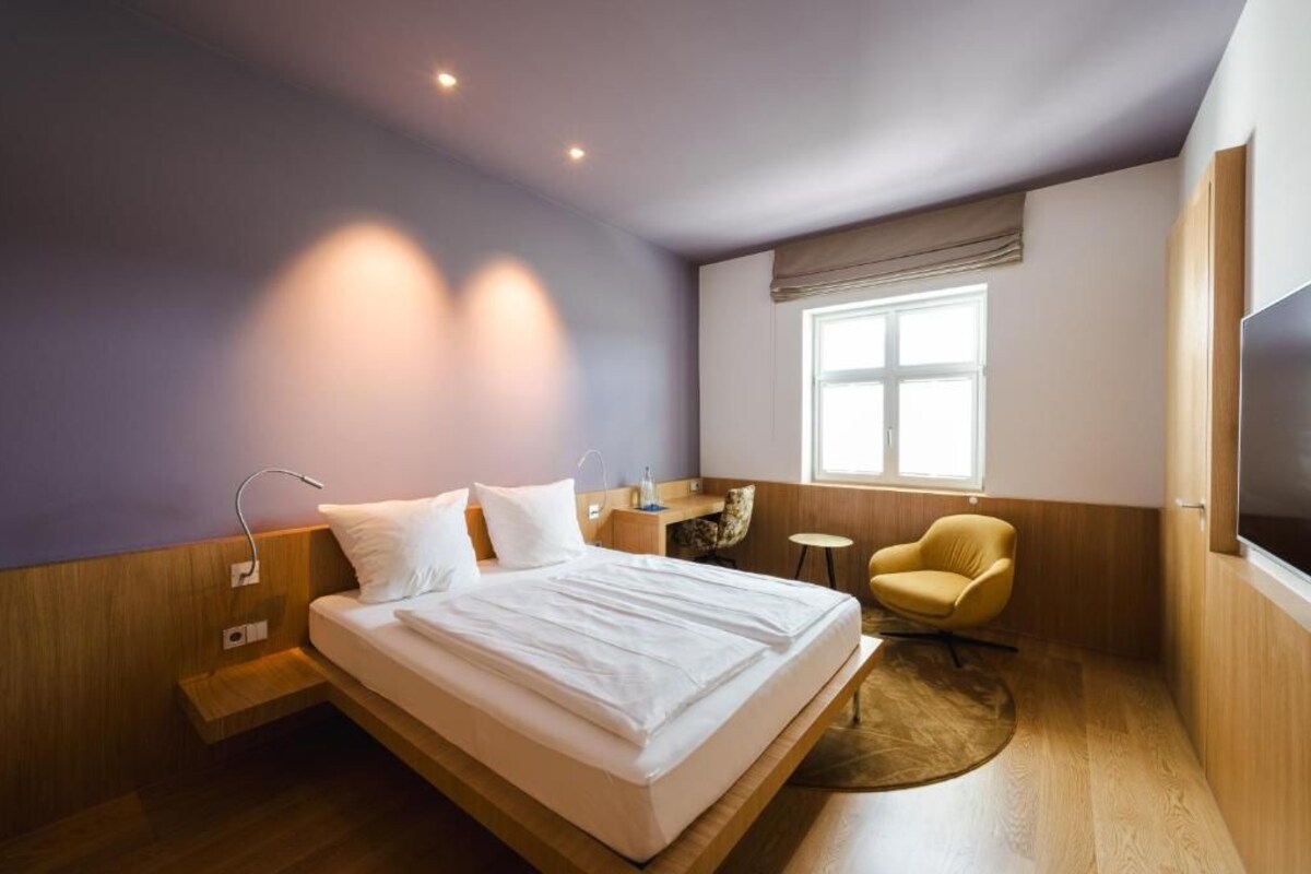 A modern hotel room with a large bed, a desk, a chair, and a TV.