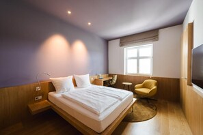 A modern hotel room with a large bed, a desk, a chair, and a TV. - das Ox (Münster)