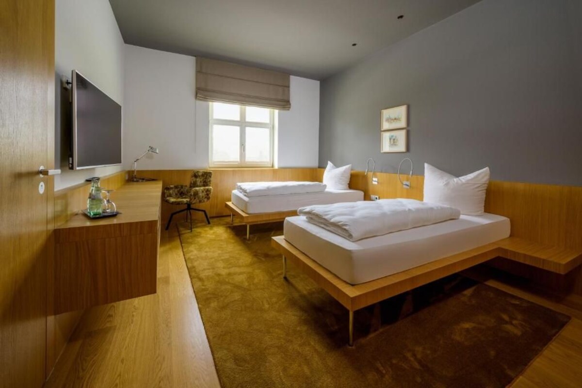 A hotel room with two beds, a desk, a TV, and a window.