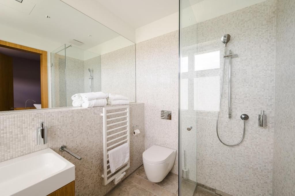 Un baño moderno con cabina de ducha de vidrio, inodoro blanco y toallero con toallas dobladas.