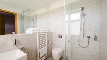 Un baño moderno con cabina de ducha de vidrio, inodoro blanco y toallero con toallas dobladas.
