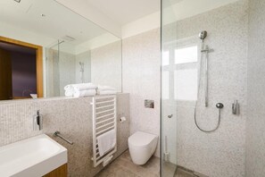 Et moderne badeværelse med en glasbrusekabine, et hvidt toilet og et håndklædestativ med foldede håndklæder.