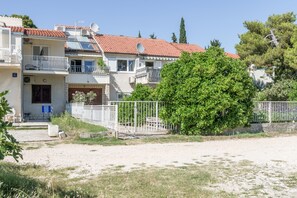 Un edificio residencial con varios balcones, patio cercado y un gran árbol al frente.