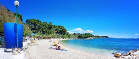 A beach with clear blue water, a few people sunbathing, and a blue lamp post.
