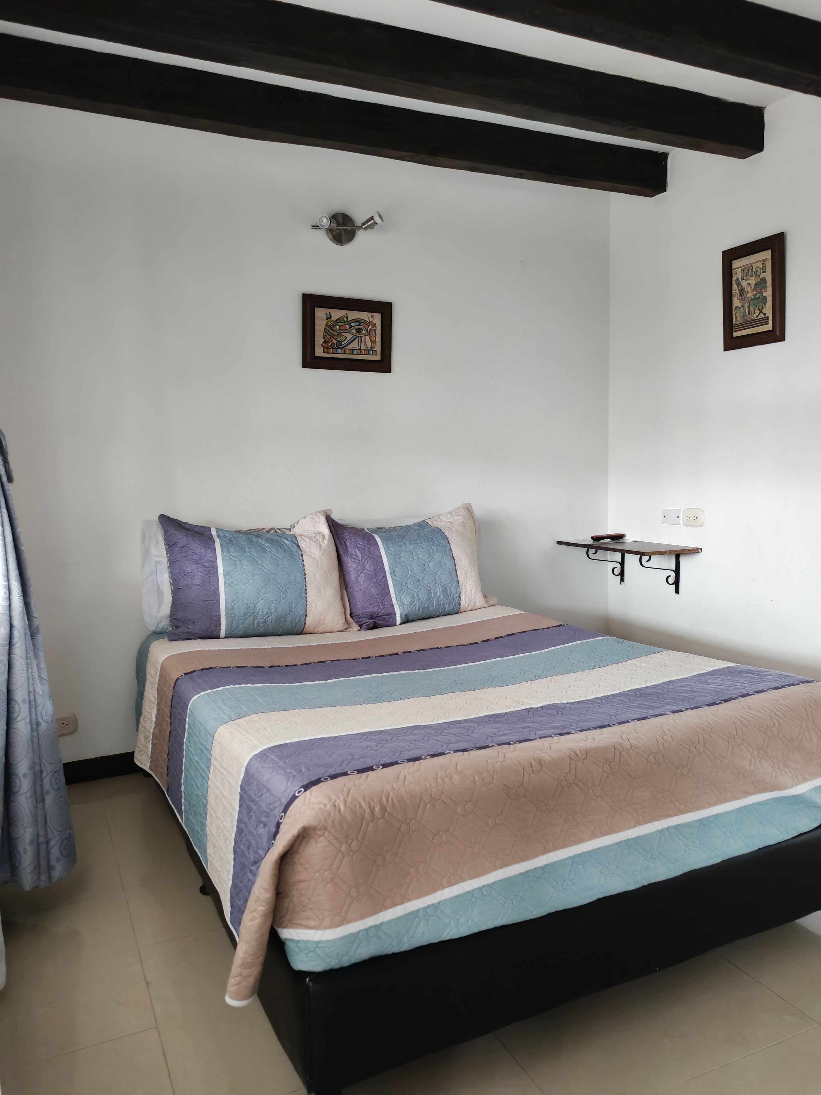 Un dormitorio con cama, mesita de noche, luz de pared y un cuadro enmarcado.
