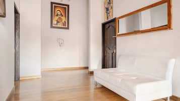 Una habitación con un sofá blanco, suelo de madera, una puerta de madera oscura y un espejo montado en la pared.