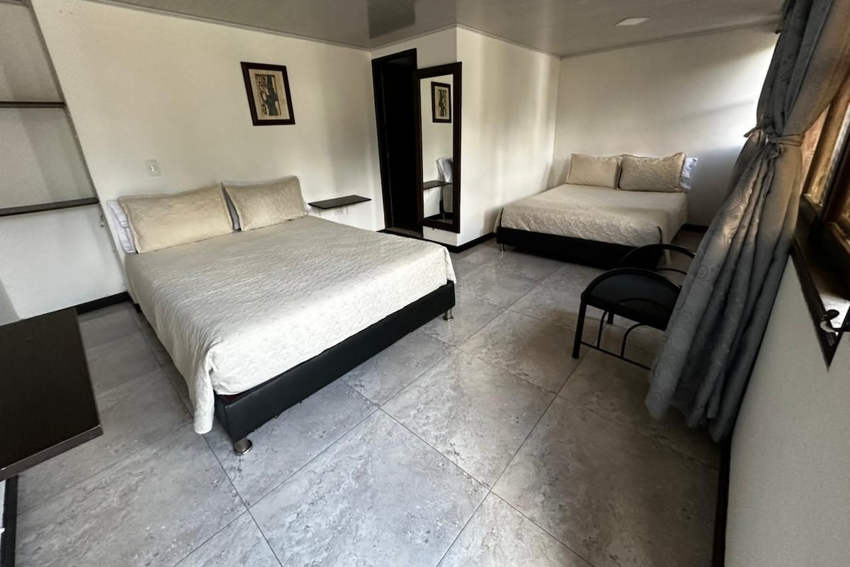 Habitación de hotel con una cama, una silla, una mesita y un espejo.