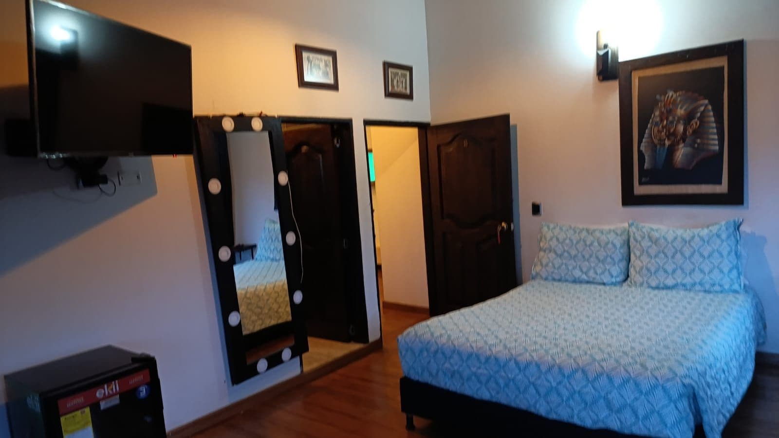 Quarto com cama, televisão, espelho e porta.