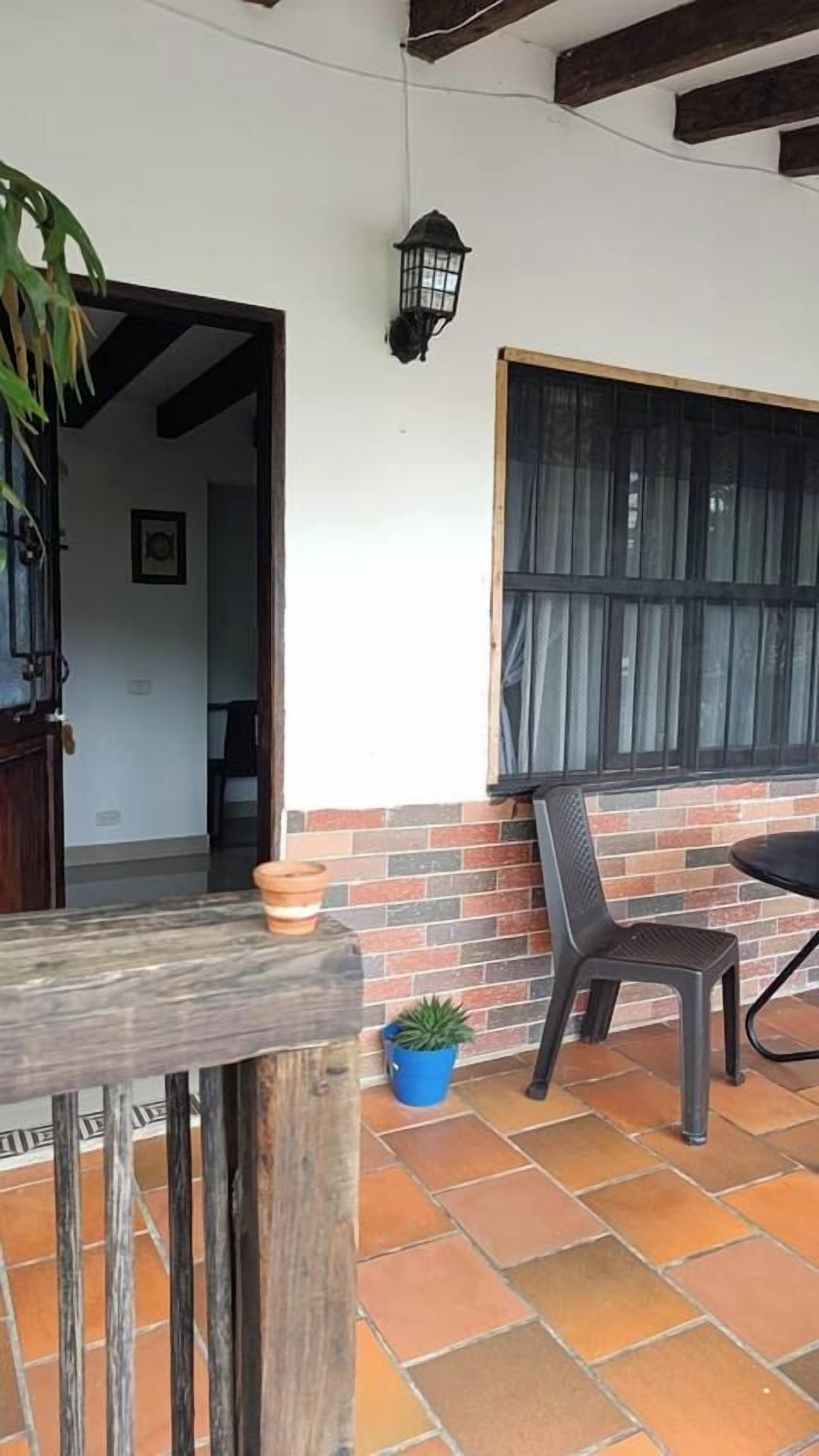 Un patio con un muro de ladrillo, una ventana con cortinas, una silla y una planta en maceta.