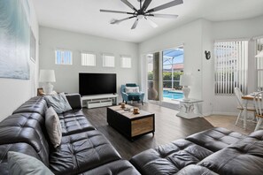 A modern living room with a leather sofa, a flat-screen TV, and a ceiling fan.