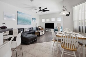 A modern living room with a black leather sofa, a dining table with white chairs, a flat-screen TV, and artwork on the walls. - Tuscan Villa for Big Families, Near Disney Parks (Davenport)