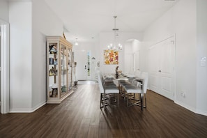 A spacious dining area with a long table and modern chairs, a glass-fronted display cabinet, and a chandelier.