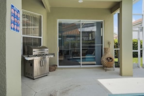 An outdoor patio with a barbecue grill, a glass door leading to a pool, and a decorative vase. - Tuscan Villa for Big Families, Near Disney Parks (Davenport)