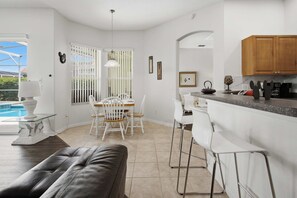 A modern kitchen with white cabinetry, a dining area with white chairs, and a pool visible through the window. - Tuscan Villa for Big Families, Near Disney Parks (Davenport)