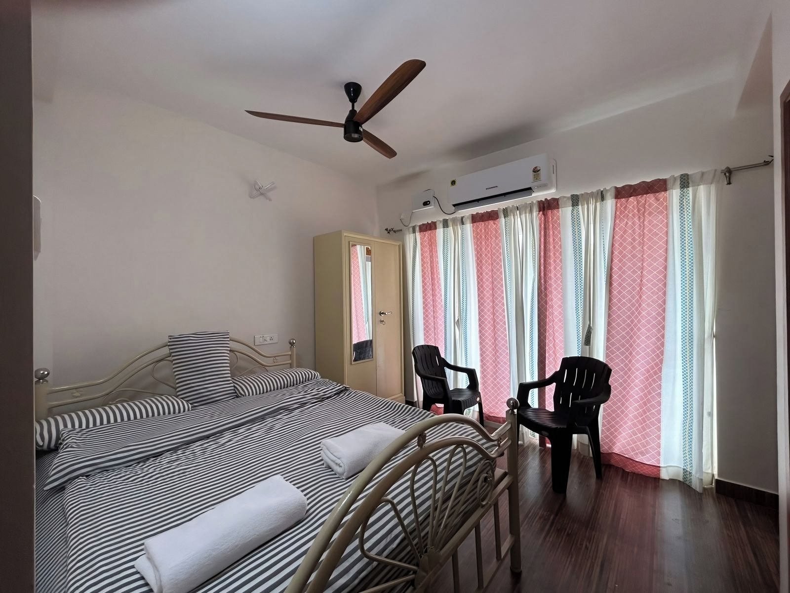 Une chambre d’hôtel comprenant un lit, deux chaises, une armoire, un climatiseur et un ventilateur de plafond.