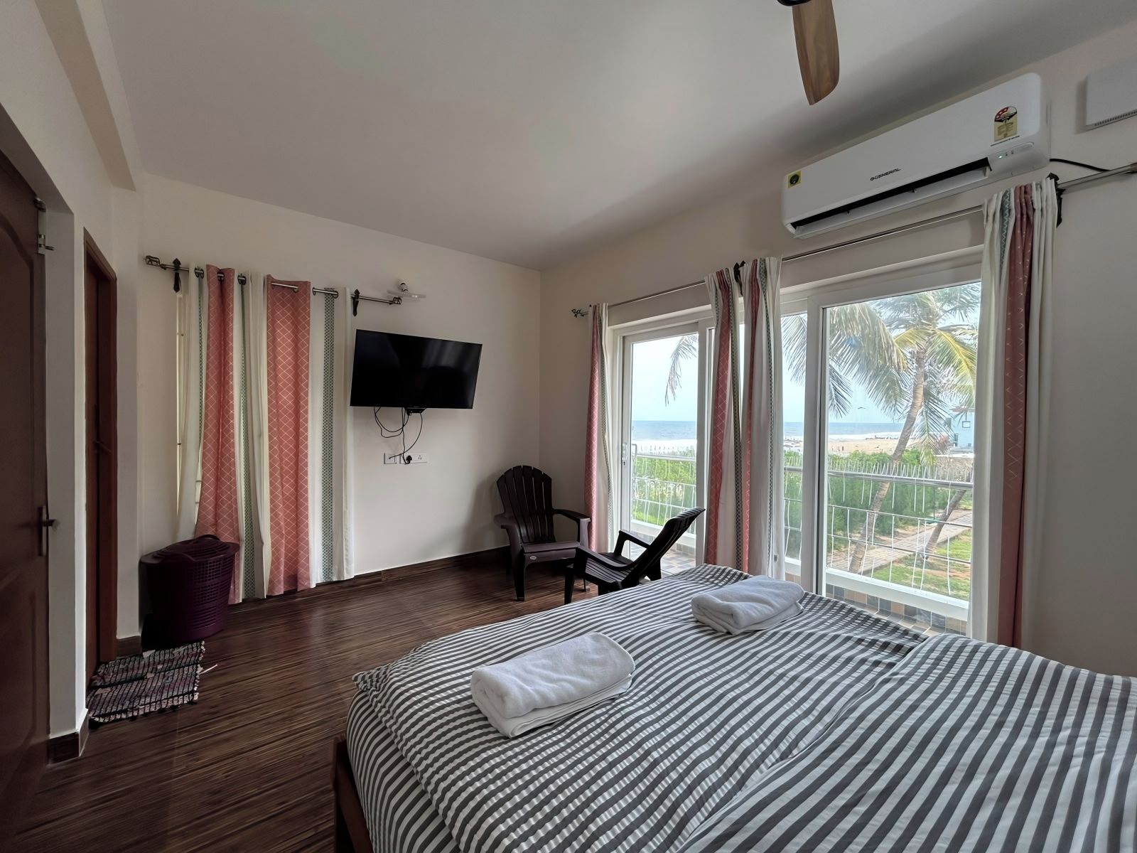 A hotel room with a bed, a chair, a TV, and a balcony with a view of the beach.