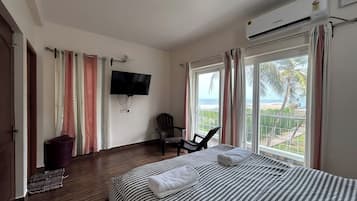 A hotel room with a bed, a chair, a TV, and a balcony with a view of the beach.
