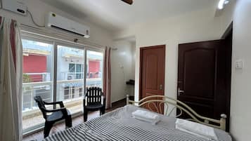 A hotel room with a bed, a chair, a ceiling fan, an air conditioning unit, and a view of the outside.