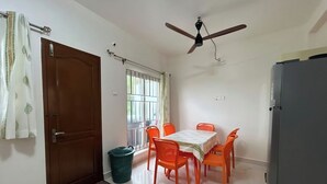Ein Zimmer mit Esstisch, Stühlen, Deckenventilator, einem vergitterten Fenster und einem Kühlschrank.
