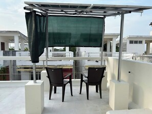 A rooftop terrace with a table and chairs, a green sunshade, and a view of surrounding buildings.