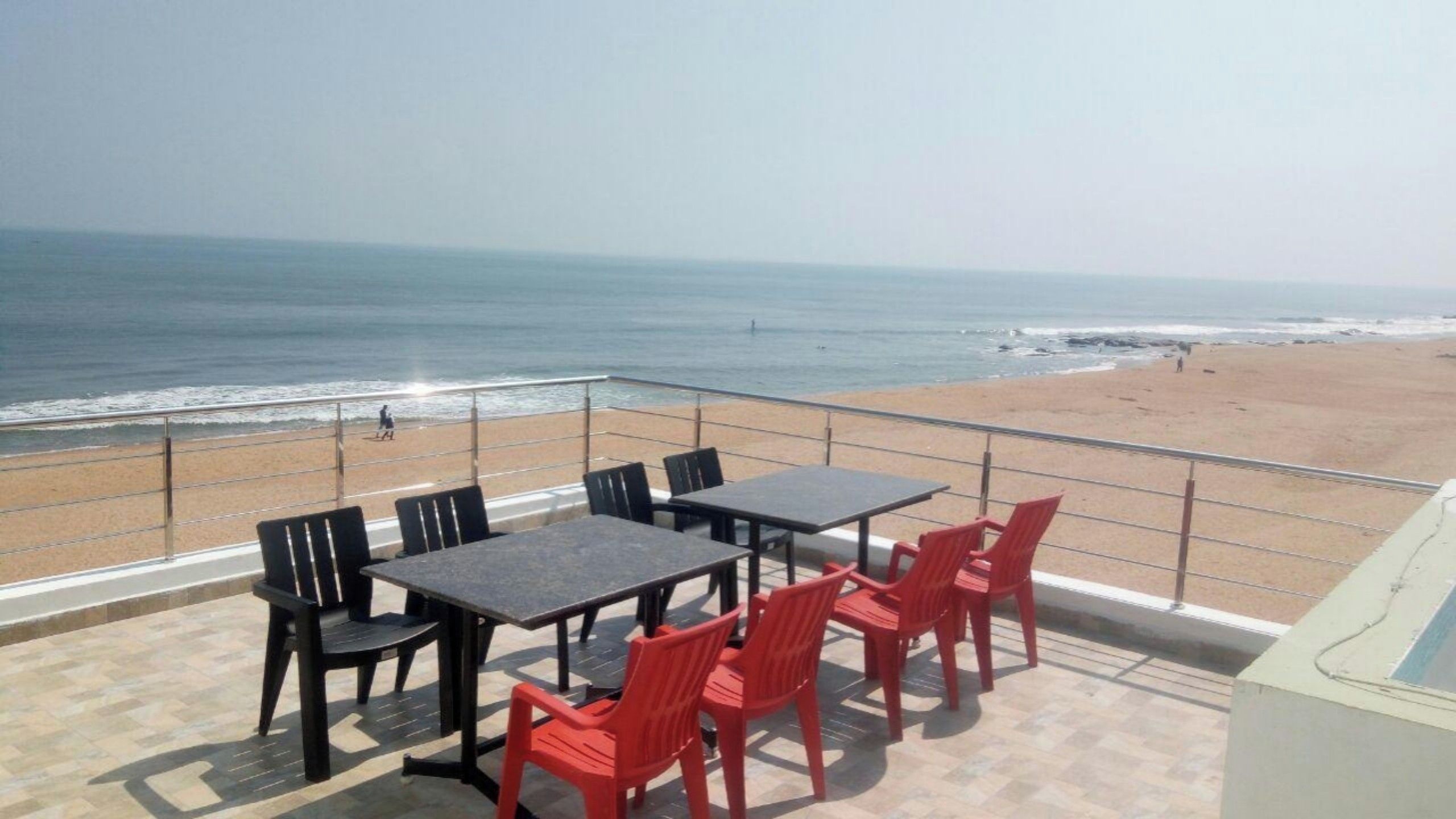 Une terrasse offrant une vue sur la plage et l’océan, avec des tables et des chaises.