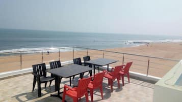 Une terrasse offrant une vue sur la plage et l’océan, avec des tables et des chaises.