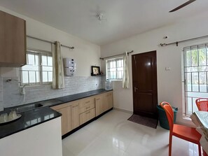 A kitchen with a sink, cabinets, a window with curtains, and a door.