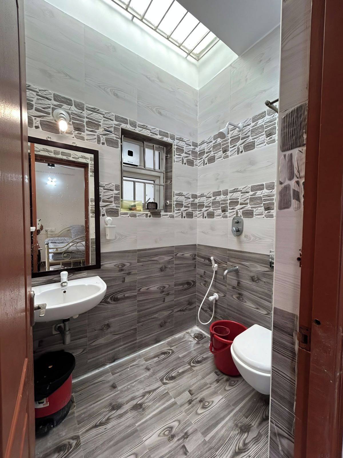 A bathroom with a skylight, a sink, a toilet, and a red bucket.