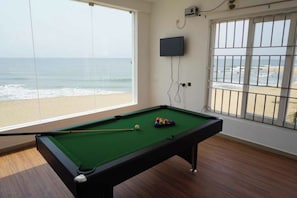 Ein Billardtisch mit Blick auf den Strand durch große Fenster.