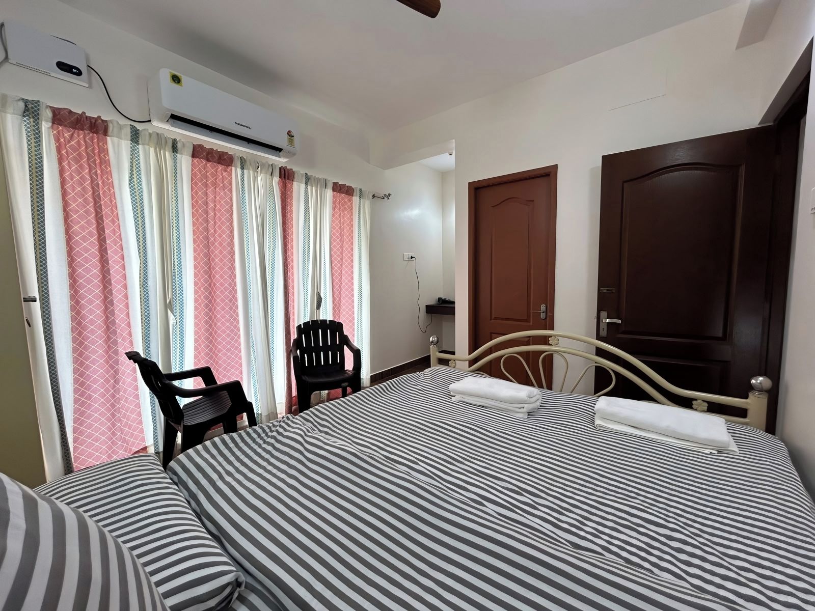 A hotel room with a bed, a chair, an air conditioning unit, and a wardrobe.