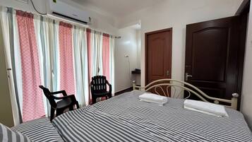 A hotel room with a bed, a chair, an air conditioning unit, and a wardrobe.