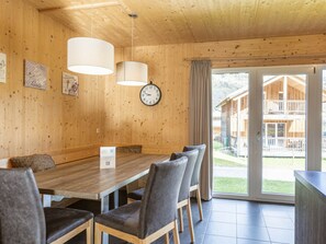 Ein Holzinnenraum mit einem Esstisch, Stühlen, einer Uhr und Blick auf ein Holzgebäude im Freien.