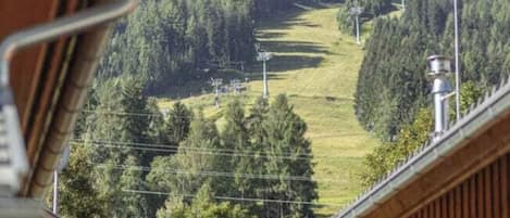 A wooden cabin with a view of a forested hill and a ski slope in the background.
