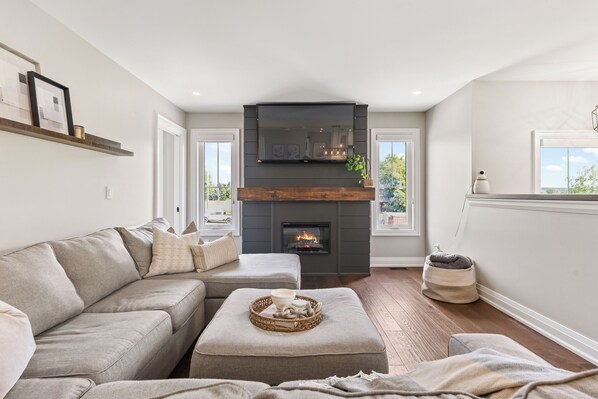A living room with a fireplace, a sofa, an ottoman, and a view of the outdoors.